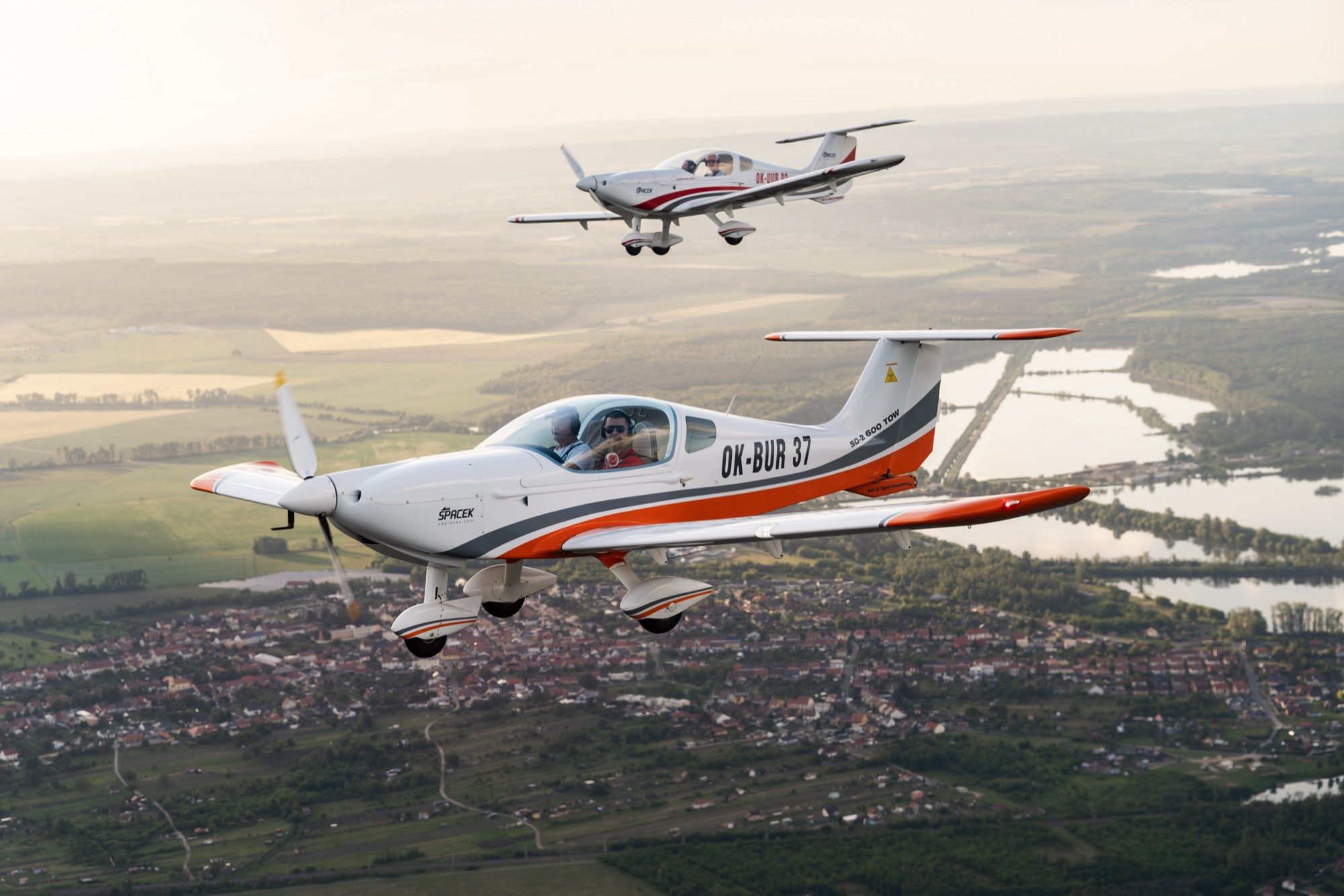 Two aircraft in formation at golden hour over lakes and countryside